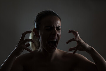 Dramatic portrait of a woman shouting and displaying claw-like gestures against a dark background