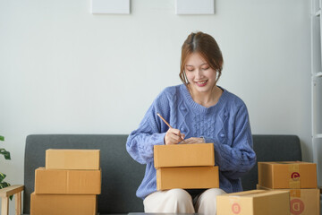 Woman packing boxes for shipping, sitting on a couch in a cozy living room, preparing parcels for delivery, smiling while working.