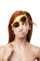 A young red-haired woman with a playful expression, wearing oversized yellow sunglasses, isolated on a white background.