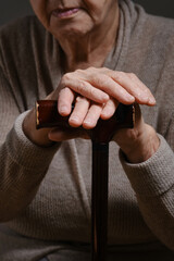 An elderly woman's hands on the handle of a cane. Hands of an elderly woman on a cane. Senior woman holding an old wood cane to support himself. Shallow depth of field