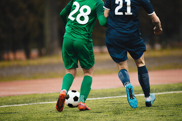 Two Adult Soccer Football Players Compete For Ball Next To Pitch Sideline. Soccer Players in Green And Blue Team In a Duel. Footballers in Jersey Uniforms