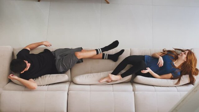 Top above view of happy couple jumping on the sofa laughing. Rest on cozy couch, celebrate move day to own home, newly married in new home. Video concept of happy young family and furniture store.