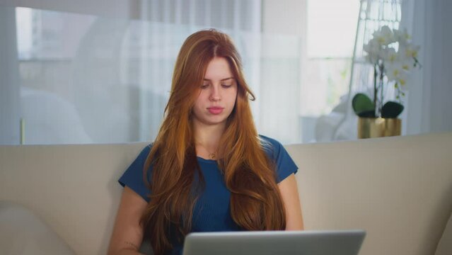 Young adult woman typing on laptop computer chatting in internet. Beautiful female using pc technology doing online job in office or browsing web sit at sofa. 