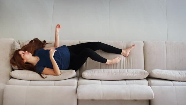 Young Woman Relaxing on a Sofa. Girl Lying on a Couch Relaxing and Watching TV at Home. Enjoying free time.