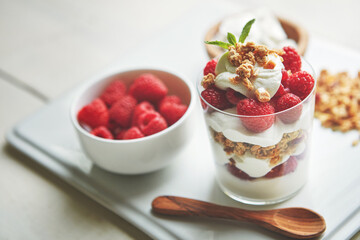 Glass, cereal and yogurt with raspberry on plate for healthy food, vegan or meal at breakfast. Fruit, fiber and dairy with spoon by clear container with protein for morning, organic nutrition or diet