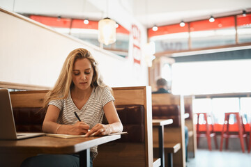 Woman, notebook and writing at coffee shop with laptop as university student for elearning or...