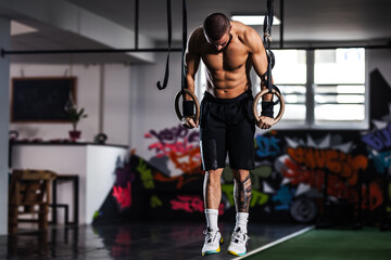 Fit young male athlete performs a muscle-up on gymnastic rings in a vibrant gym