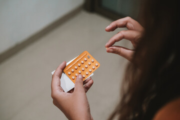 Close up of a hands young woman holding a package of birth control pills. She takes out one pill...
