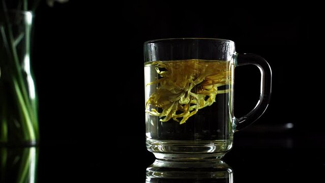 Stirring a teaspoon into a transparent mug with a flower. Dark scene. 4 k