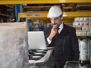 Middle-aged Caucasian warehouse manager working on a personal computer and thinking about shipment in a large warehouse distribution center.