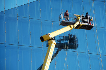 Cleaner worker using a cherry picker to clean a glas facade of a contemporary office building