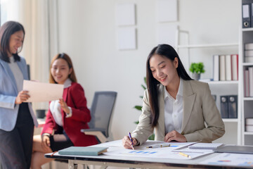 Fototapeta premium Group of businesswomen collaborating in a modern office. Focused on teamwork, documents review, and effective business planning.