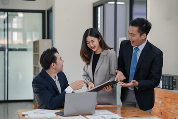 Three business professionals engage in a discussion in an office setting, reviewing documents and working together on a project.