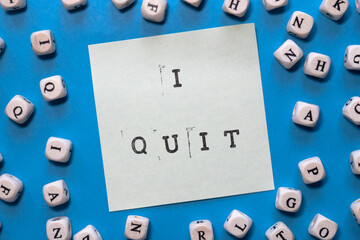 i quit stamped on white sticky note on a bright blue background with cubes with letter around it