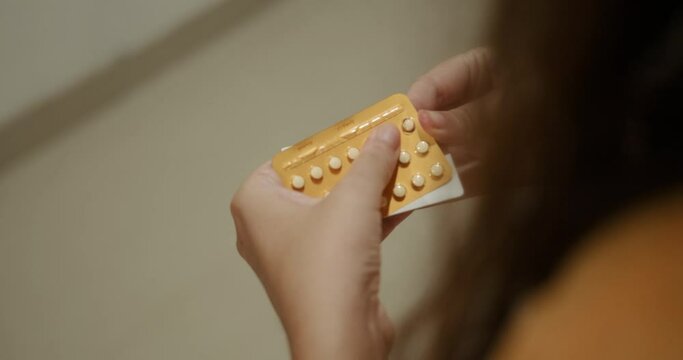 Close up of a hands young woman holding a package of birth control pills. She takes out one pill and takes it. Contraceptives and birth control. Childfree people.