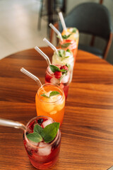 Fruit drinks with berries and ice in glass glasses and straws on a wooden table.