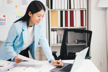 Beautiful Asian business woman uses digital tablet and laptop to do remote work at the office, online seminar or video call.