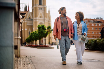 Obraz premium Happy couple of tourists talking while walking on city street.