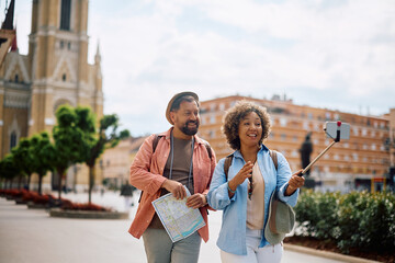 Happy couple of tourists taking selfie while sightseeing in city.