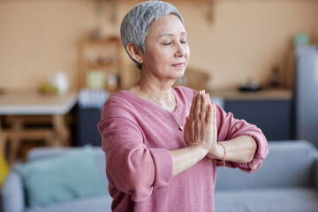 Waist up portrait of blissful senior woman enjoying yoga practice at home and meditating copy space