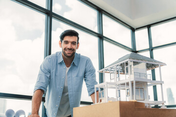 Portrait of smart engineer in casual outfit smiling at camera while inspect house model. Skilled...