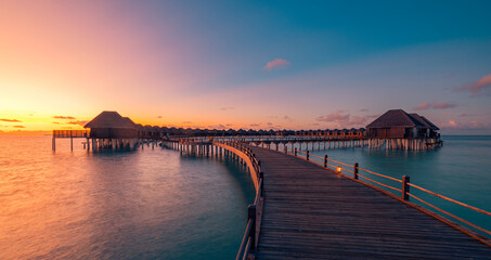 Fototapeta premium Amazing travel beach luxury landscape. Beautiful Maldives tourism sunset seascape view. Horizon colorful sea sky, over water villa pier pathway led lights. Tranquil island, vacation travel background