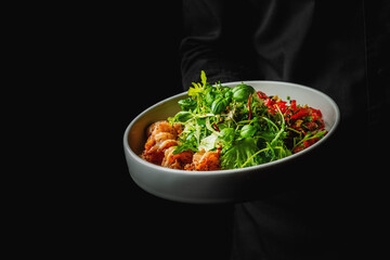 Fresh mixed salad with grilled shrimp served in a white bowl against a dark background. Healthy meal option.