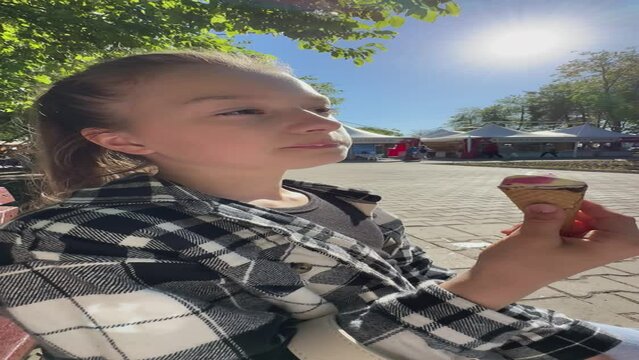 happy child eats ice cream while relaxing in the park on a summer day, girl 11 years old with dark hair eats colorful ice cream, having fun in the amusement par