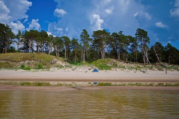 Relaxing by the sea in a tent. View of the coast from the sea. Dunes and pine trees. Baltic Sea. Sandy shore.