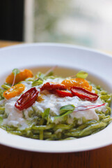 Close-up of Italian trofia pasta with pesto, burrata cheese and cherry tomatoes served on a white plate. Italian (Ligurian) cuisine, selective focus.