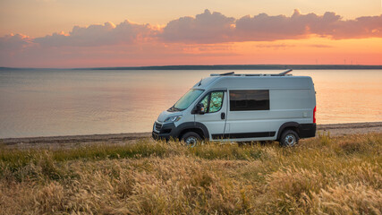 Obraz premium panoramic view to white camper van on the coast in calm morning before sunrise