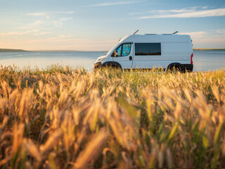landscape view to white camper van on the coast through yellow grass in sunset time in summer day