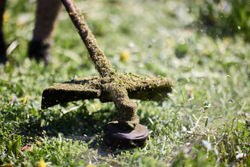 Casing and rod of working gasoline line trimmer are covered with chopped grass, close-up.