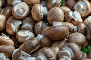 A full frame photograph of chestnut mushrooms on a market stall, with selective focus