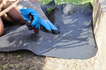 Laying an anti-weed mat in the garden together with paving stones and decorative pebbles