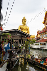 The Giant Budah in the skirts of the river and the canoes passing by xthe water next to a house on the shore