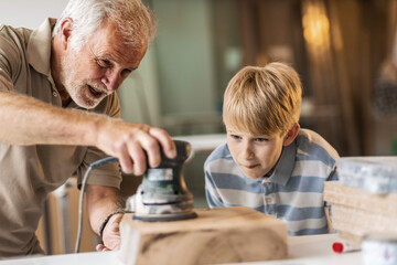 A grandfather teaches his grandson how to fix furniture in his carpenter workshop.