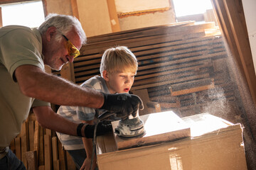A grandfather teaches his grandson how to fix furniture in his carpenter workshop.