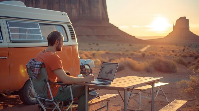 Man working on laptop computer with camper van in campsite in trip