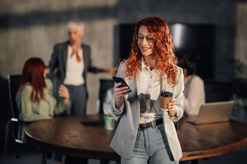 Smiling professional businesswoman texting on cellphone in meeting room