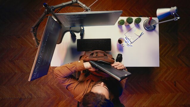 Top down view of software programmer finishing remote job shift, packing backpack, leaving office after finishing project. Aerial shot of IT admin putting laptop in bag, sitting up from desk chair