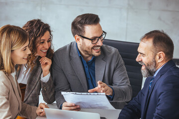 A group of business professionals, displaying a blend of ethnicities, collaborate eagerly around a document. Their professional attire and tools like a laptop suggest an office environment.