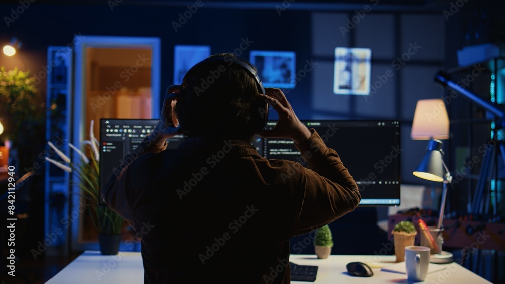 Poster engineer wearing headphones while using coding to fortify security, remotely working for it company.