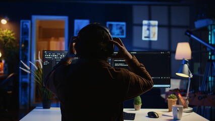Engineer wearing headphones while using coding to fortify security, remotely working for IT...