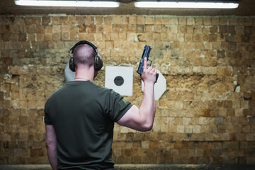 An athletic man with a modern pistol in his hand at a shooting range.
