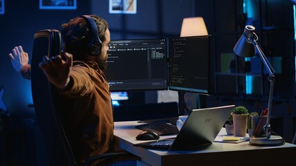 Software programmer taking break from coding, putting headphones on and stretching on desk chair...