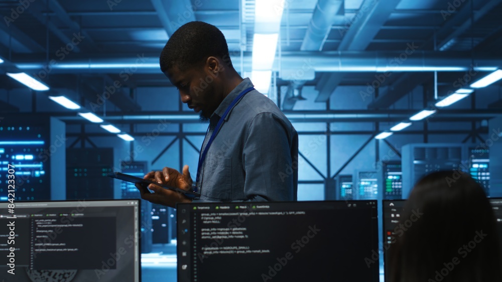 Poster technician doing system analysis using tablet, doing needed adjustments in supercomputers server far