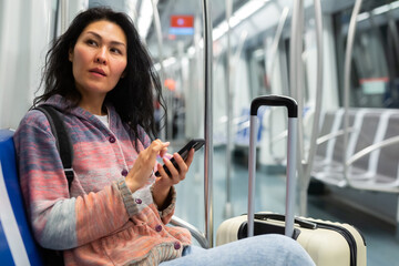 Positive female passenger with smartphone moving on subway train, using public transport in big city