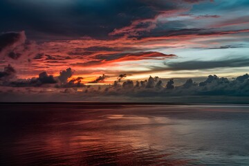 Vibrant sunset sky reflecting on calm waters with scattered clouds and horizon silhouette