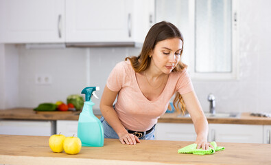 Focused young girl housewife in casual clothes cleaning table at kitchen